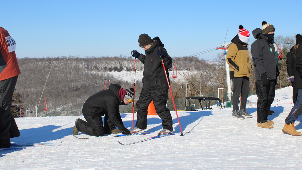 people on a ski slope maiking adjustments to skis of a student